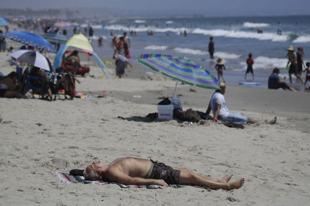 FILE - In this Sunday, July 12, 2020, file photo, a man lies on the beach amid the coronavirus pandemic in Santa Monica, Calif. California faces a heat wave Friday, Aug. 14, 2020, that could bring dangerously high temperatures throughout the state, along with the threat of wildfires and spreading coronavirus infections as people flock to beaches and recreation areas. (AP Photo/Marcio Jose Sanchez, File)