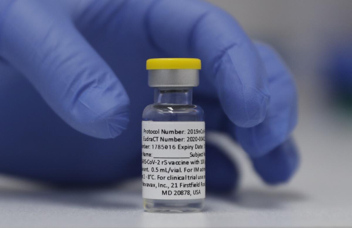 Closeup of a hand in a blue plastic glove around a small vial.