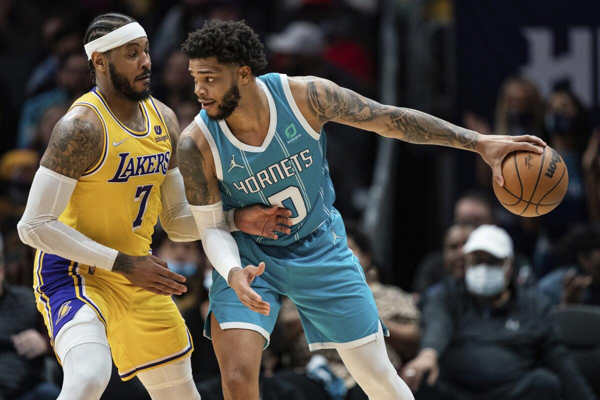 A Lakers player, left, guards a Hornets player palming a basketball.