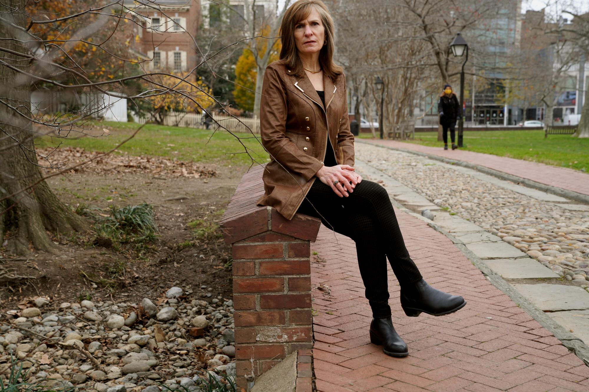 Margaret Cronan, former news director at CBS-owned station in Philadelphia, sits outdoors on a low brick wall.