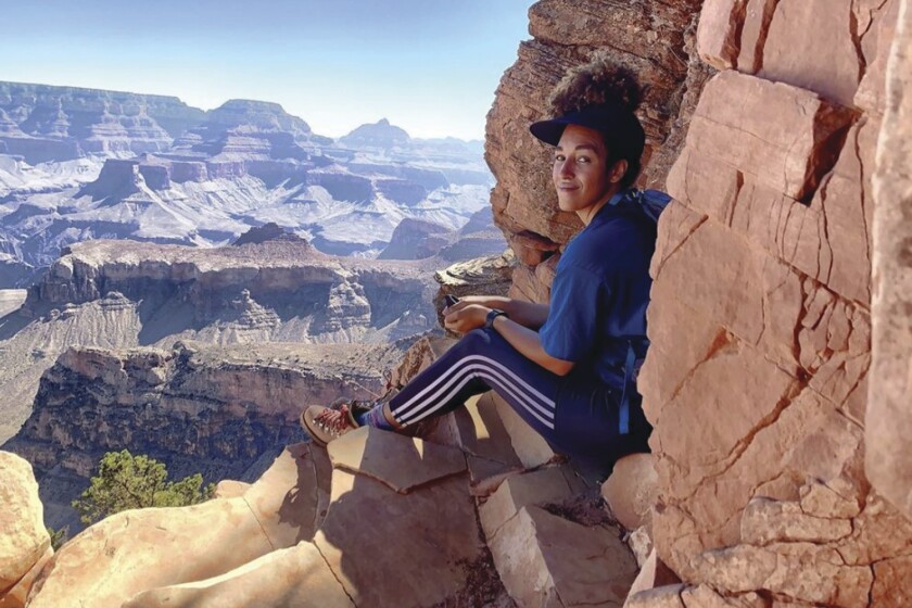 A woman sits on a rock outcropping with a stunning rocky landscape in front of her.