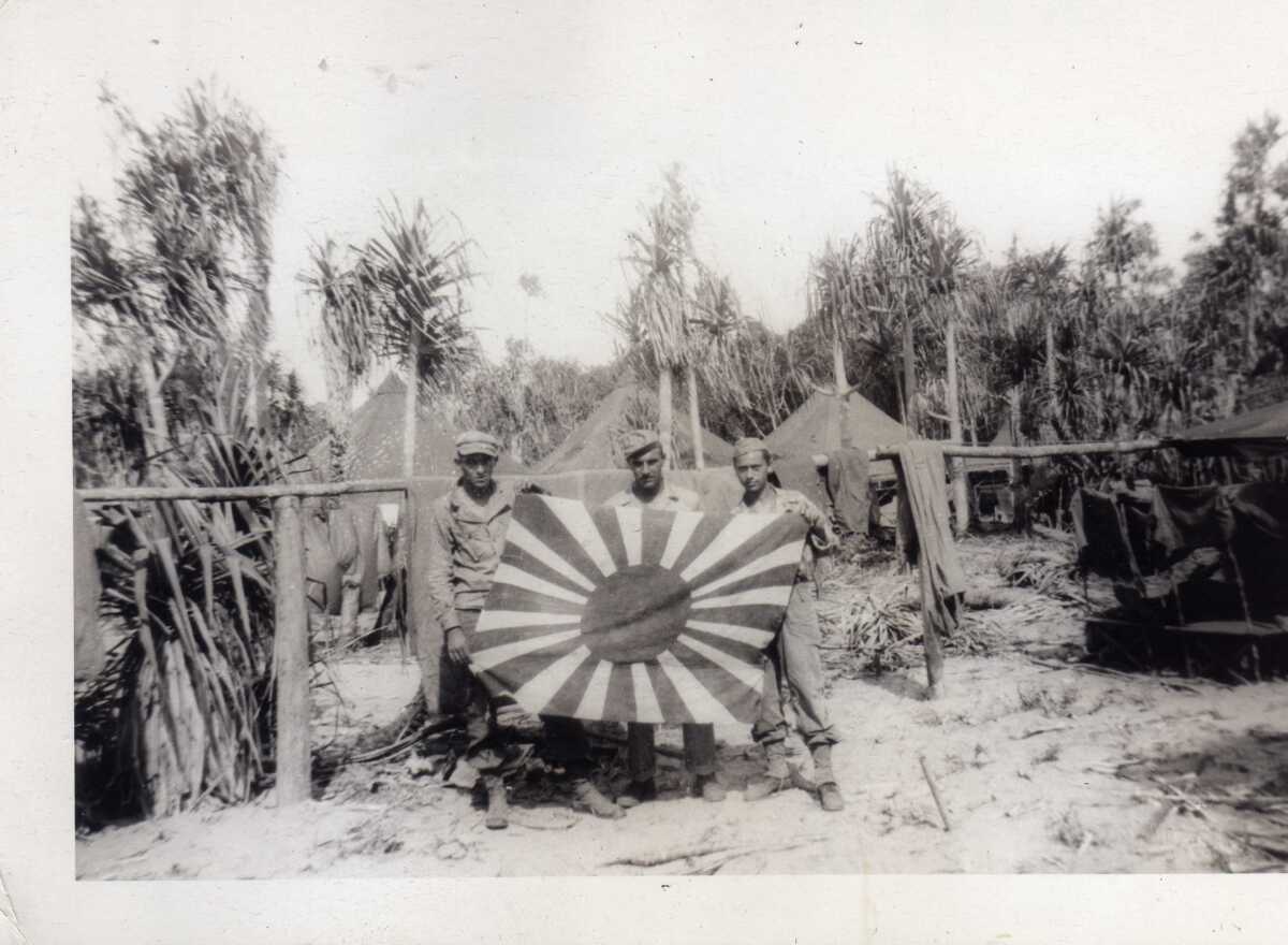 Private First Class Ernest Racer, left, stands with other soldiers and a captured Japanese flag during WWII.