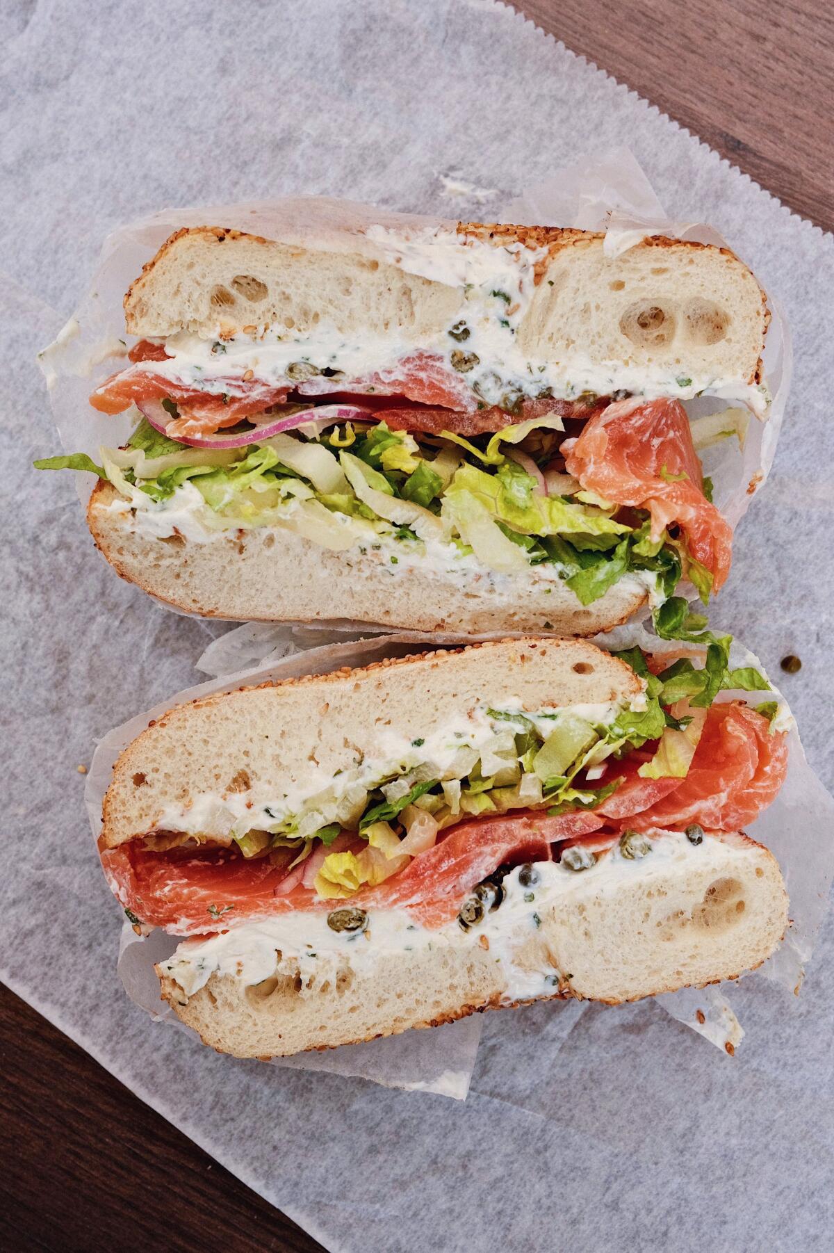 Two halves of a lox and cream cheese bagel sandwich with tomato, lettuce and red onion