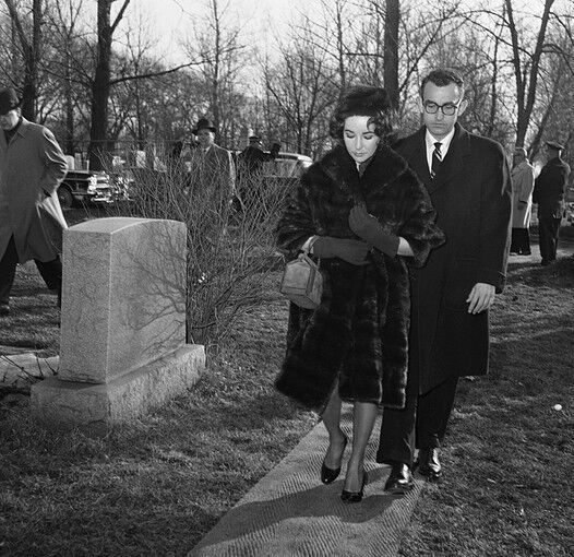 Elizabeth Taylor, accompanied by her physician, Dr. Rexford Kennamer, walks through Waldheim Cemetery in near Chicago where she attended a ceremony dedicating the grave marker of her late husband Mike Todd. Prim and proper in the 1950s, with a ladylike box bag and gloves.