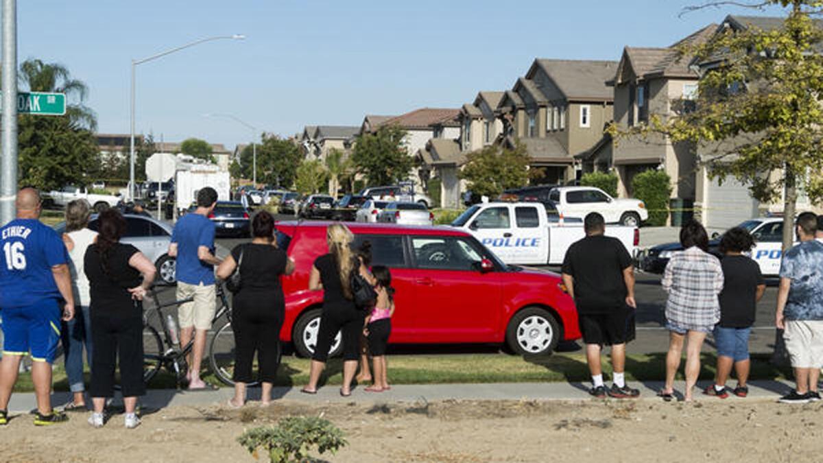 A small crowd gathers near a home where five people were found dead in Modesto.