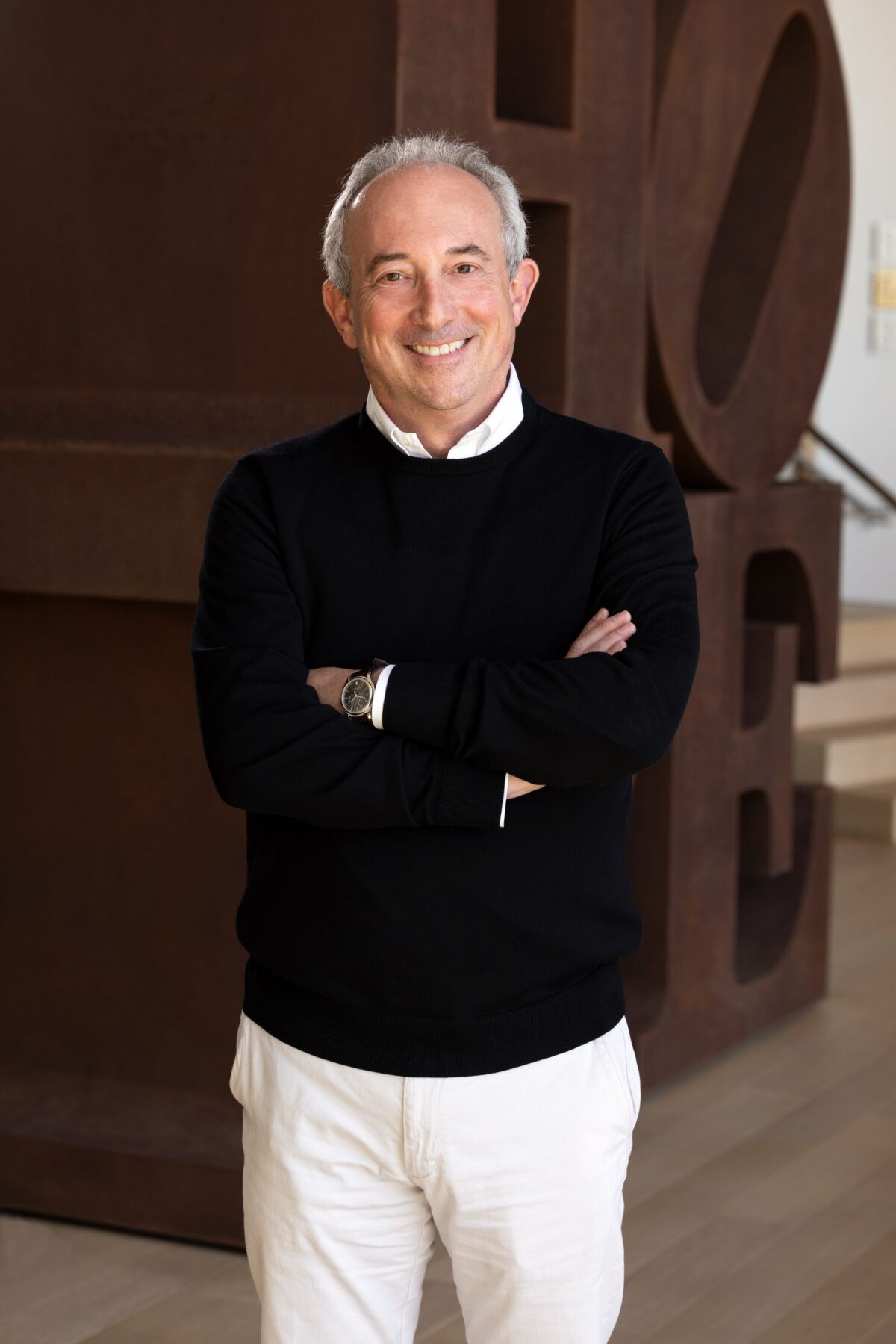 A smiling Dr. David Agus wearing a black crewneck sweater over a white dress shirt with off-white pants