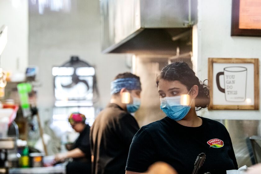 ANAHEIM, CA - APRIL 17: Nora Hawari, along with her brother Kareem and mother Nesrine Omari, work to fulfill customers orders from behind a recently installed plastic shield inside Kareem's Falafel on Friday, April 17, 2020 in Anaheim, CA. Originally founded by their parents 25 years ago, siblings Nora and Kareem Hawari are now working to keep their family business afloat during the Coronavirus pandemic. (Mariah Tauger / Los Angeles Times)