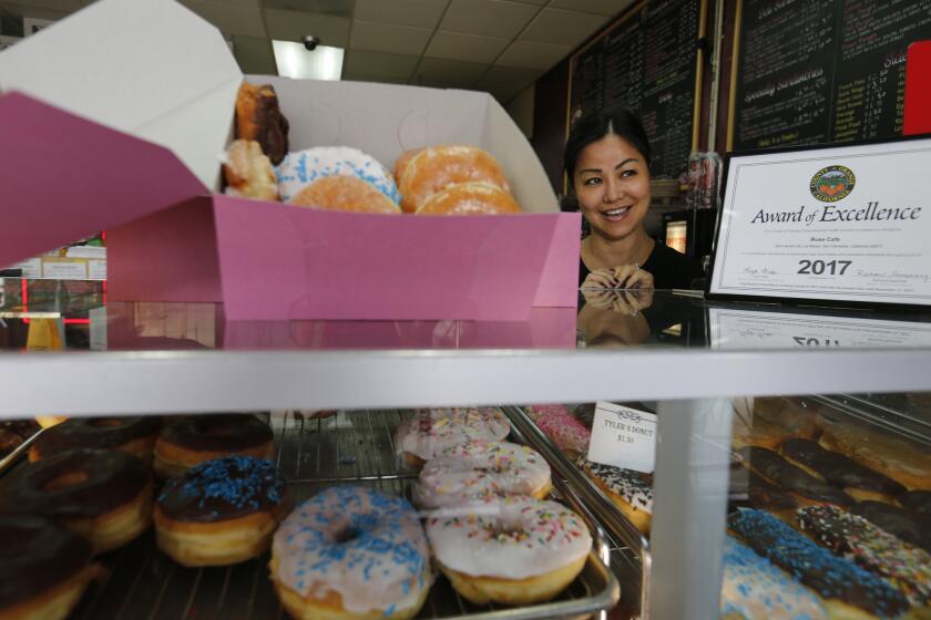 SAN CLEMENTE, CALIF. -- WEDNESDAY, MAY 10, 2017: Susan Lim, a Cambodian-American-owner of Rose Donuts & Cafe, serves doughnuts at the San Clemente store on May 10, 2017. New York has their blue, paper coffee cups. Los Angeles has the pink donut box. The cardboard containers are a staple of life here, as familiar as Vin Scully and freeway chases. Yet they can only exist because L.A. is the epicenter of the mom-and-pop donut shop. On the East Coast, Dunkin Donut boxes are ubiquitous. The pink box craze happened by chance several decades ago when a Cambodian American donut maker requested discount packaging. (Allen J. Schaben / Los Angeles Times)