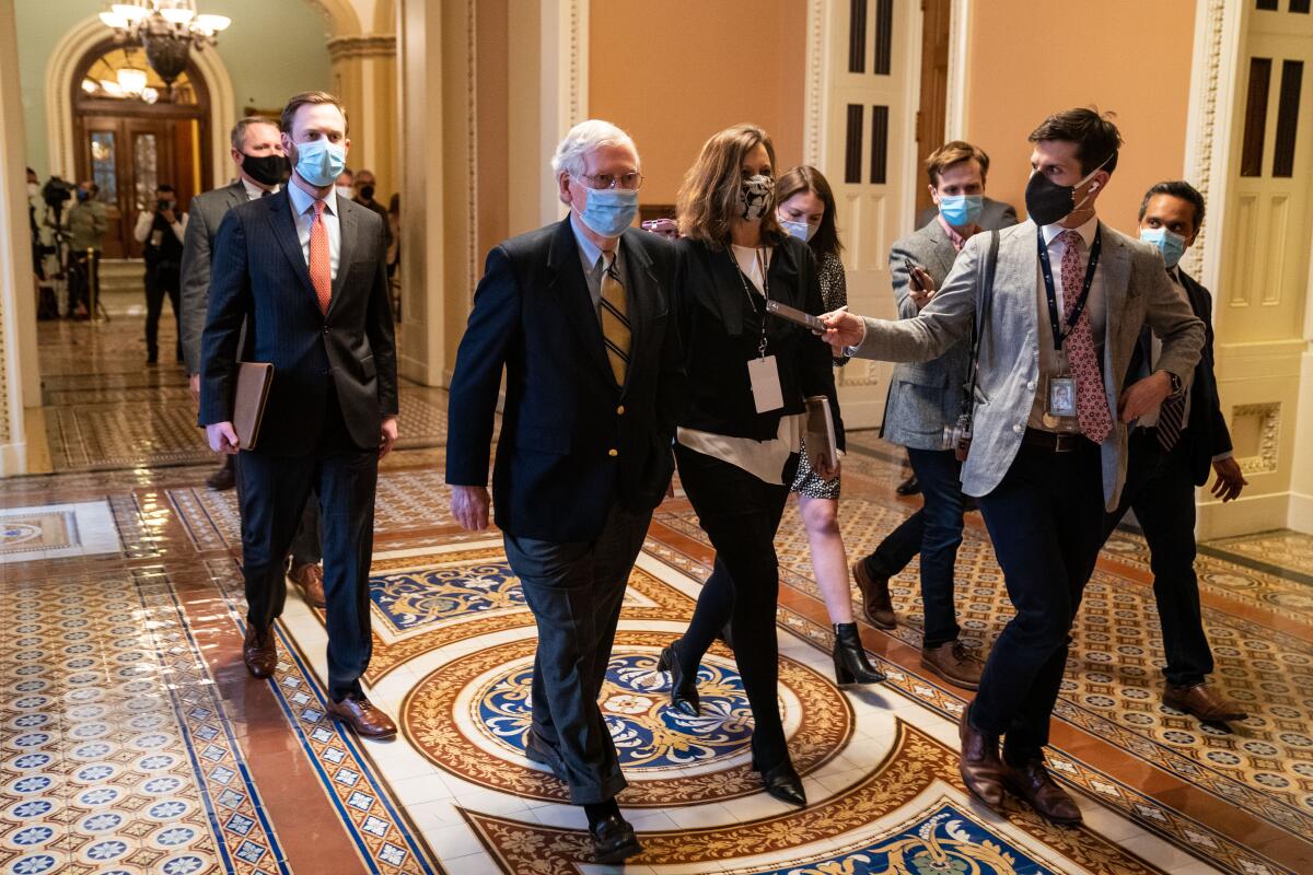 Senate Minority Leader Mitch McConnell walks down a hallway with others.
