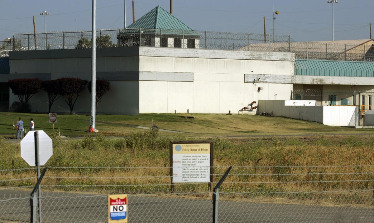 A prison wall rises behind a barbed wire fence