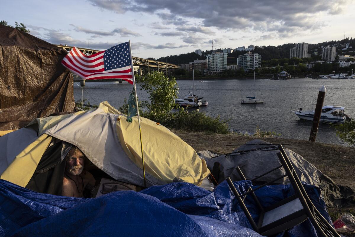 A homeless man sits in his tent with a river view in Portland.