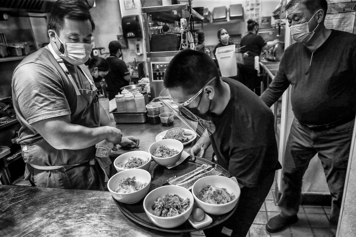 Chef Erwin Tjahyadi, left, and his father, Tjhing Sen, flank server Elver Gonzalez, picking up a tray of food.