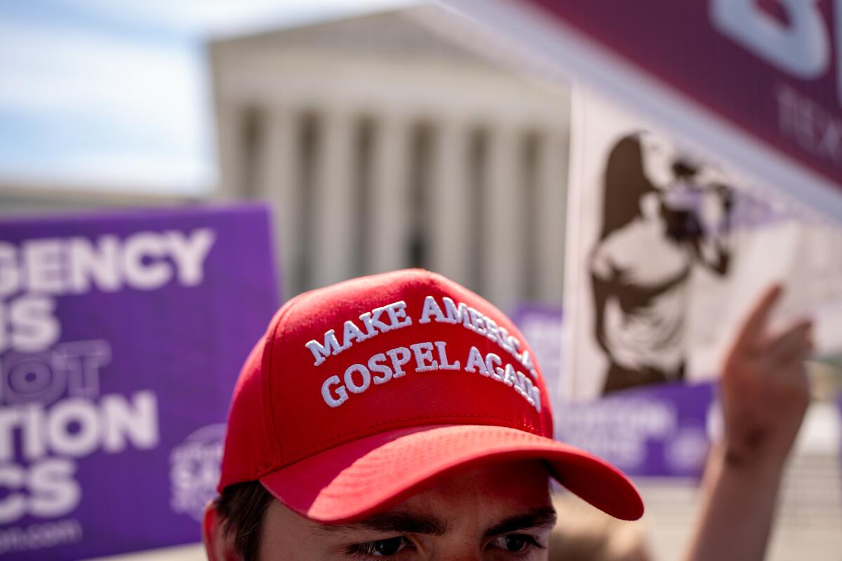 A man in front of the Supreme Court with a red baseball cap that says "Make America gospel again"