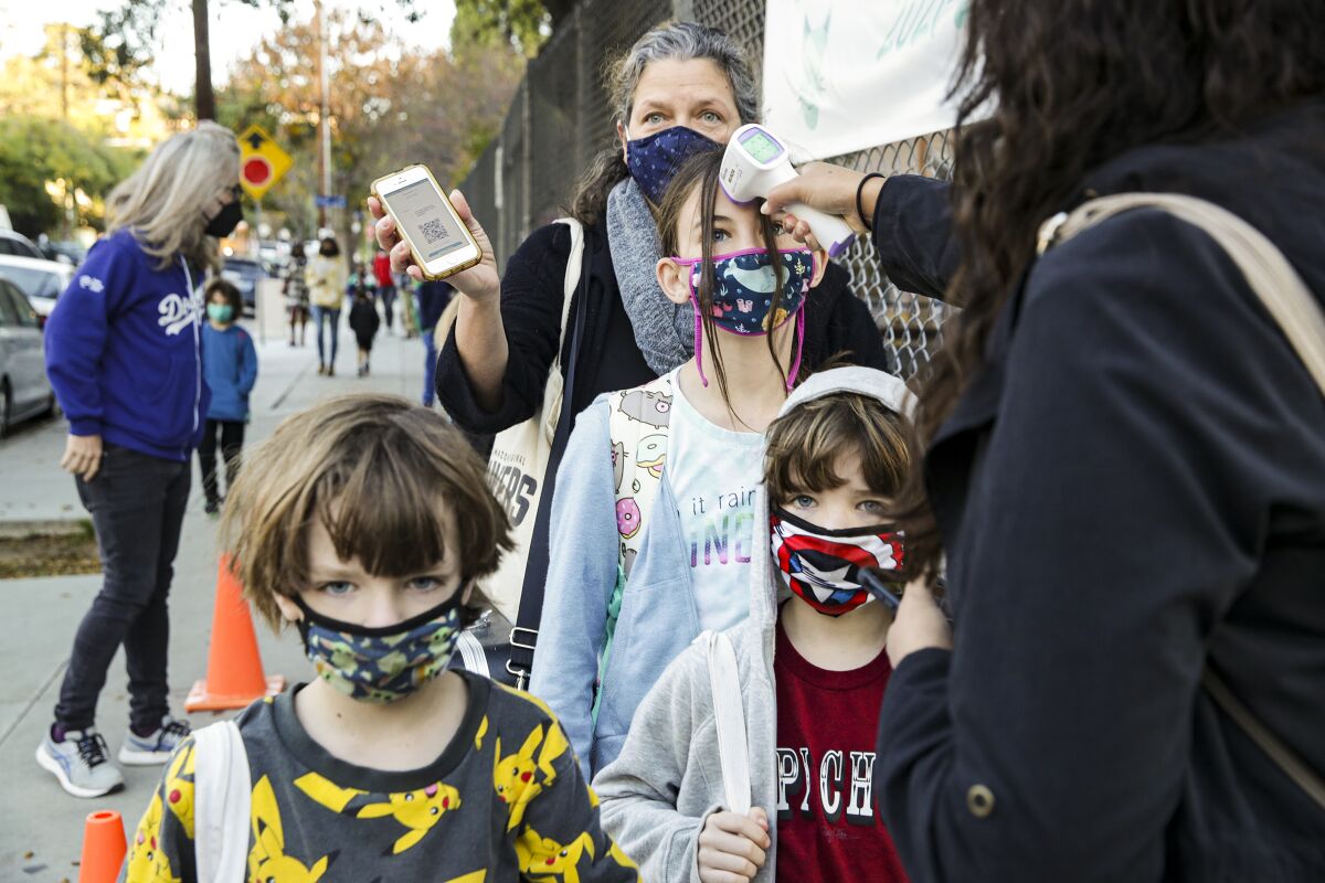 Students in masks have their temperatures taken outside school