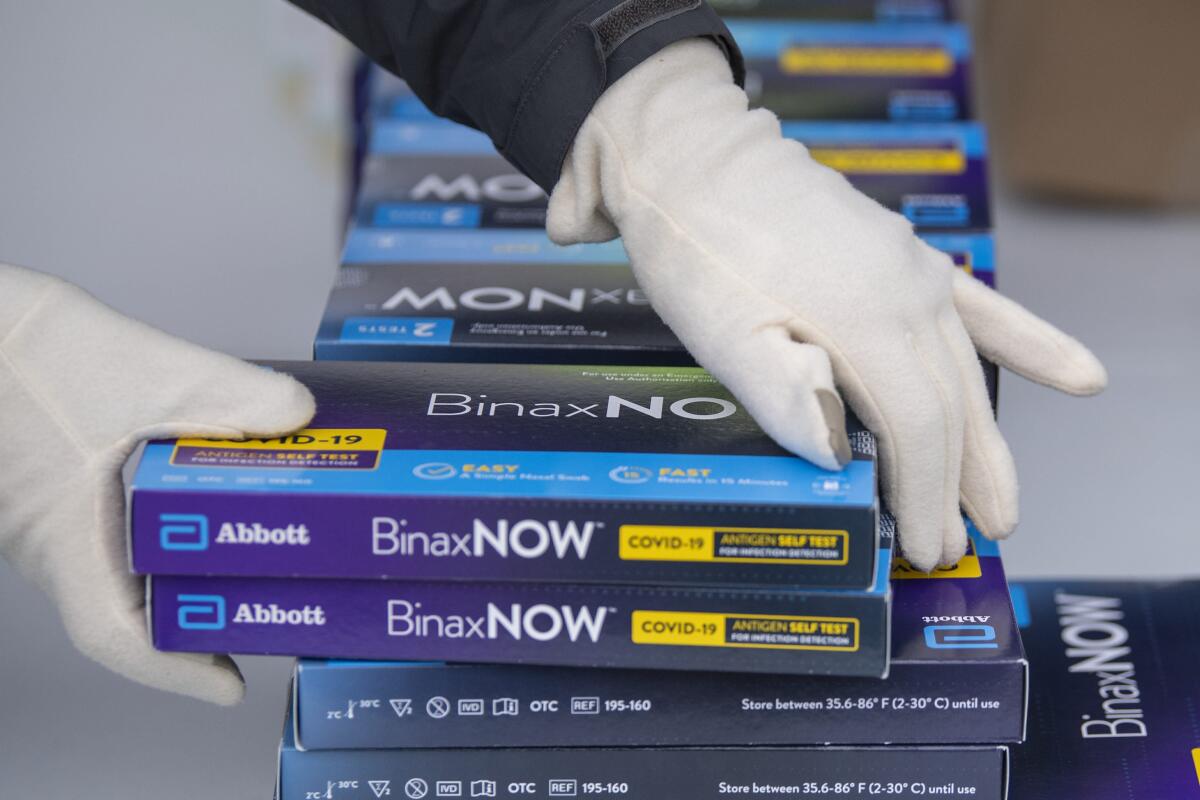 A worker picks up two COVID-19 test kits from a stack.