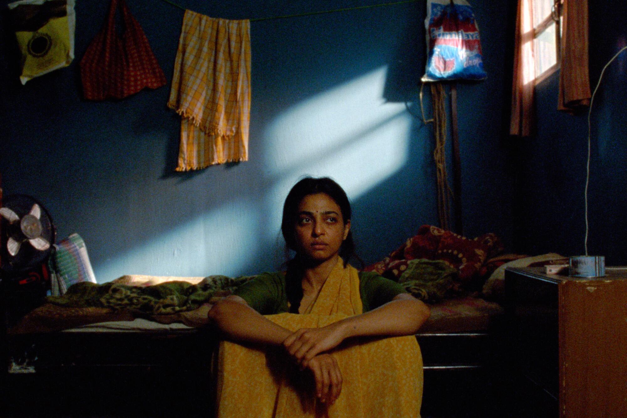 A woman sits alone in a bedroom, thinking.
