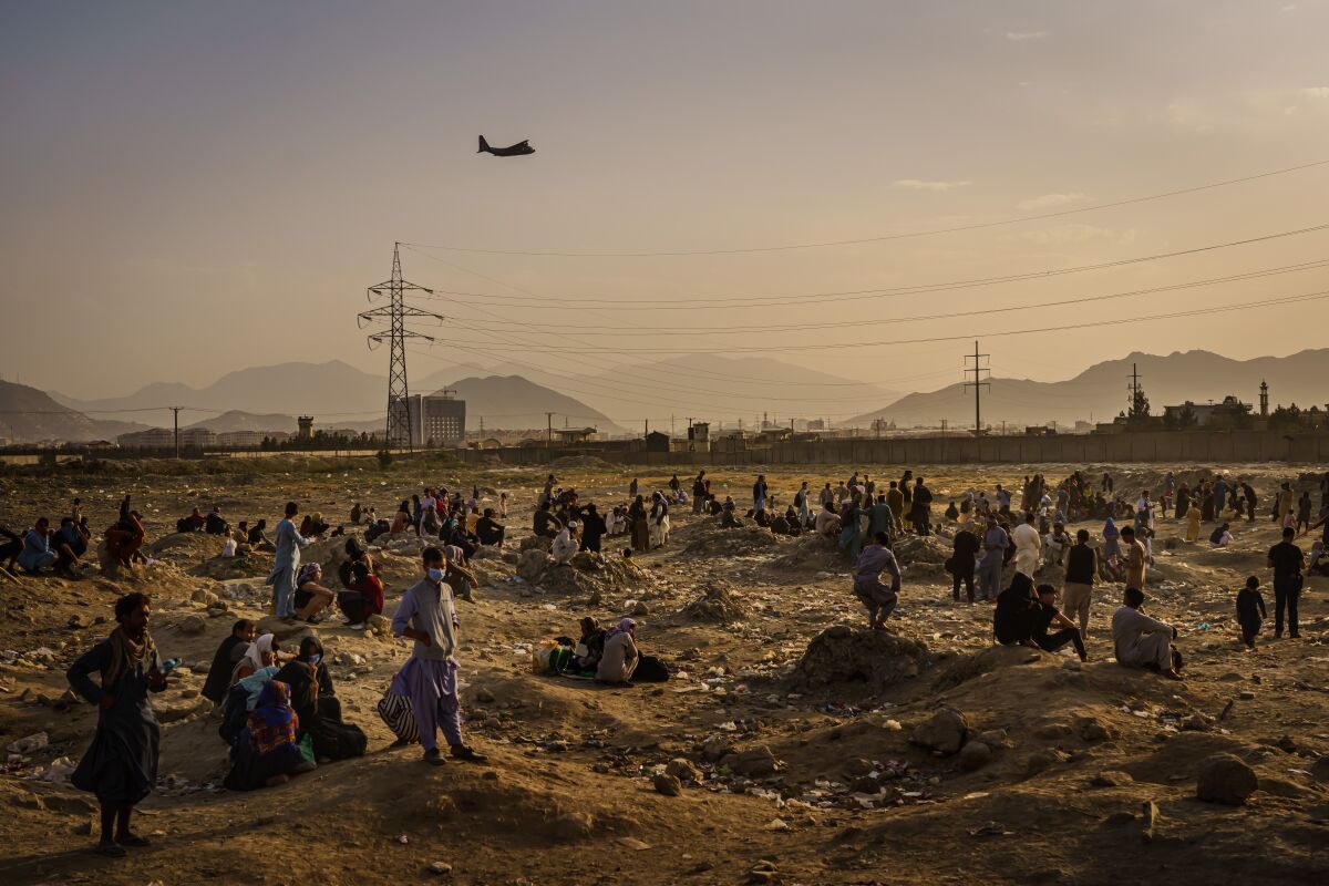 People stand in a barren field as a plane flies overhead.