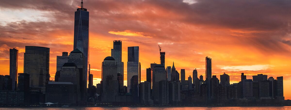 The sun rises behind the New York City skyline, seen from Jersey City, N.J.
