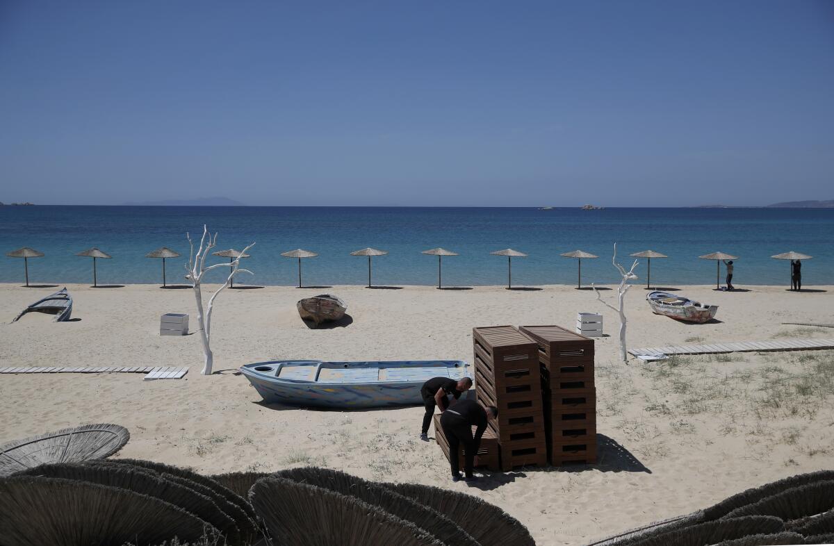 Workers arrange sunbeds as others install umbrellas at Plaka beach on the Aegean island of Naxos, Greece, Wednesday, May 12, 2021. With debts piling up, southern European countries are racing to reopen their tourism services despite delays in rolling out a planned EU-wide travel pass. Greece Friday became the latest country to open up its vacation season as it dismantles lockdown restrictions and focuses its vaccination program on the islands. (AP Photo/Thanassis Stavrakis)