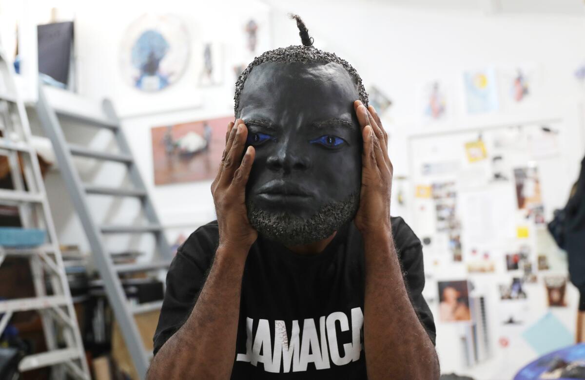 A person in a black T-shirt holds a sculpted mask of a face in front of his own face.