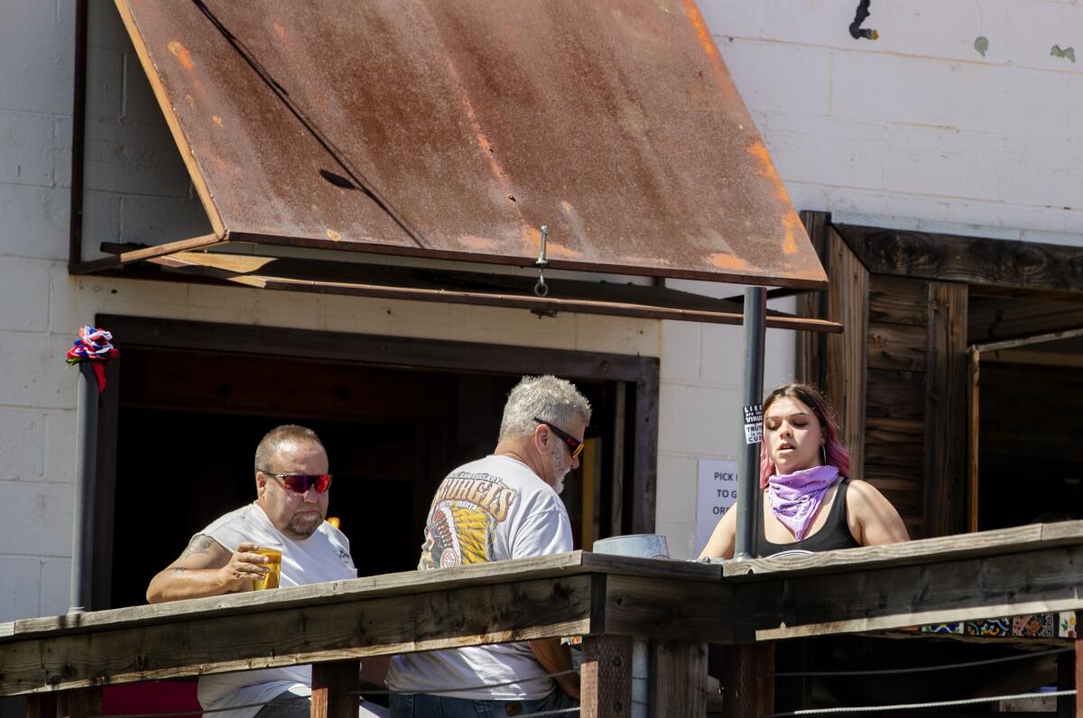 Customers and a waitress ignore social distancing and the wearing of masks on the patio at the recently opened Nomads Canteen.