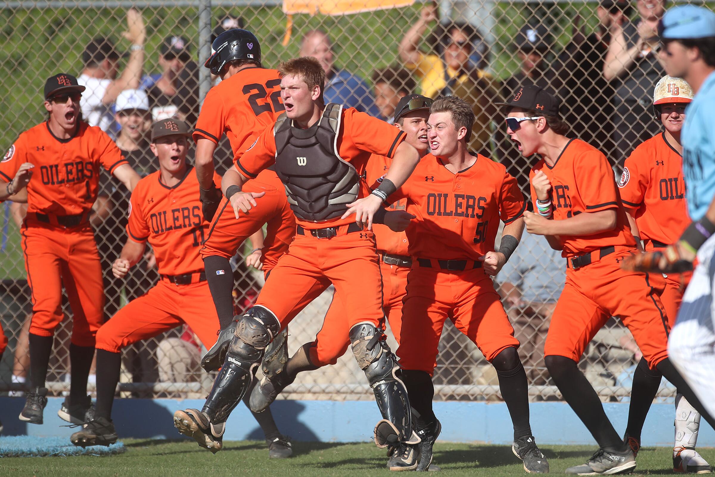 Trent Grendlinger (28) of Huntington Beach, with catchers vest, leads the collective cheer after teammate Nate Cox (22) crossed home plate for go ahead score during the second round of the Div-1 baseball playoffs against Villa Park on Tuesday.