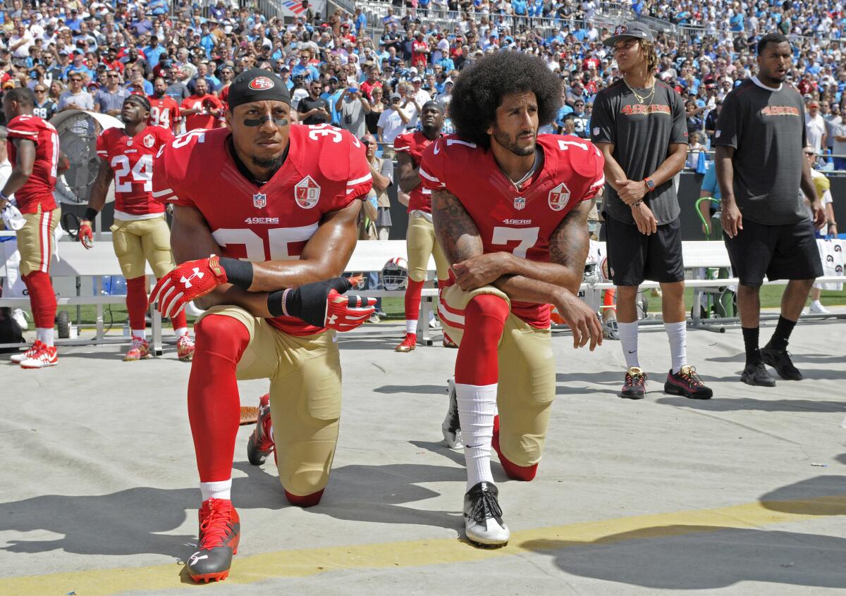 Two 49ers players in red jerseys kneel before the beginning of a football game.