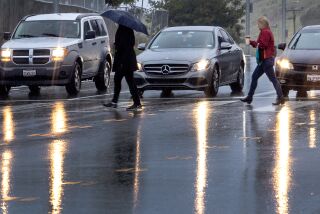 Los Angeles, CA - March 21: Pedestrians cross the road in the rain in El Sereno Tuesday, March 21, 2023. (Allen J. Schaben / Los Angeles Times)
