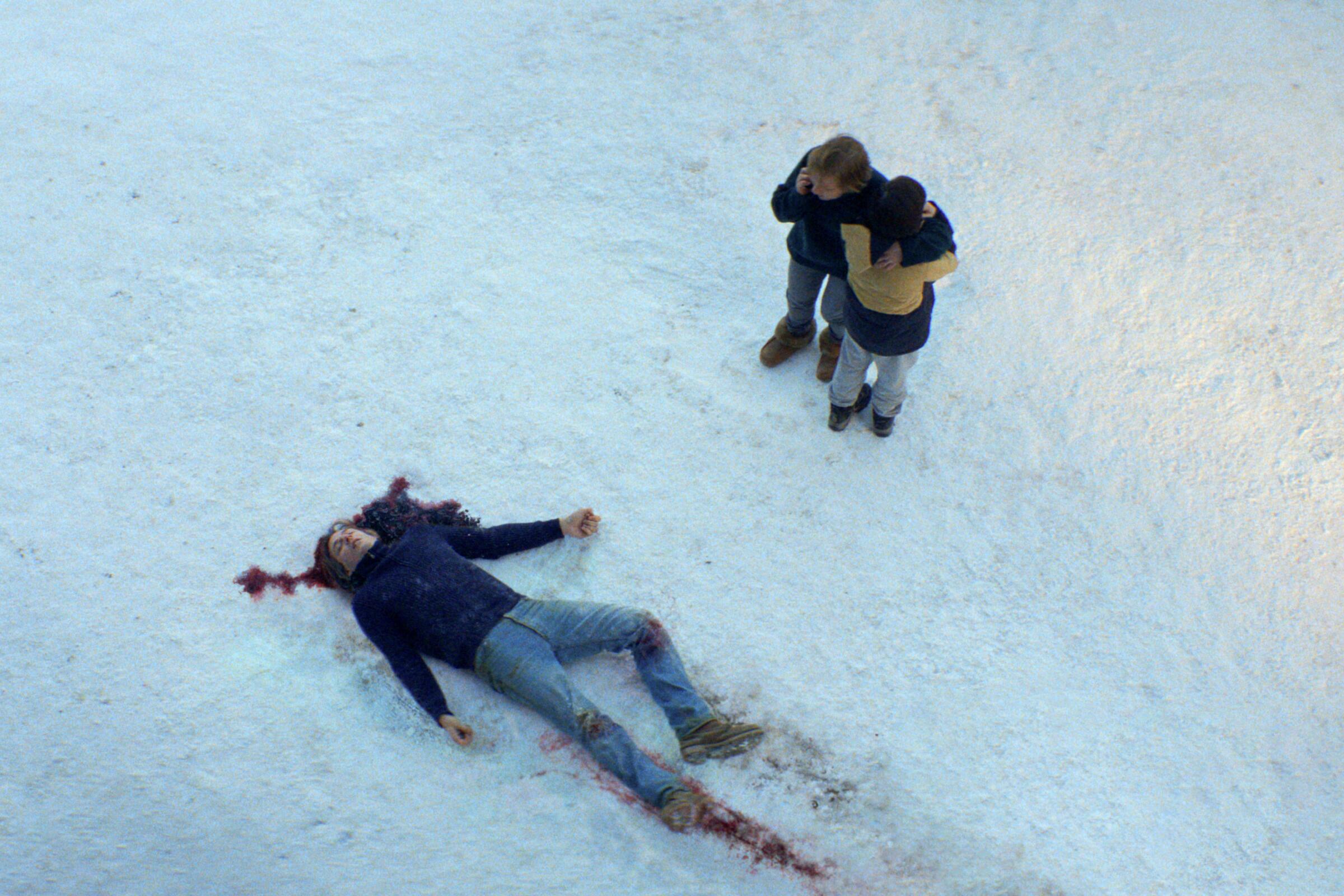 Two people stand over a body bleeding in the snow in "Anatomy of a Fall."