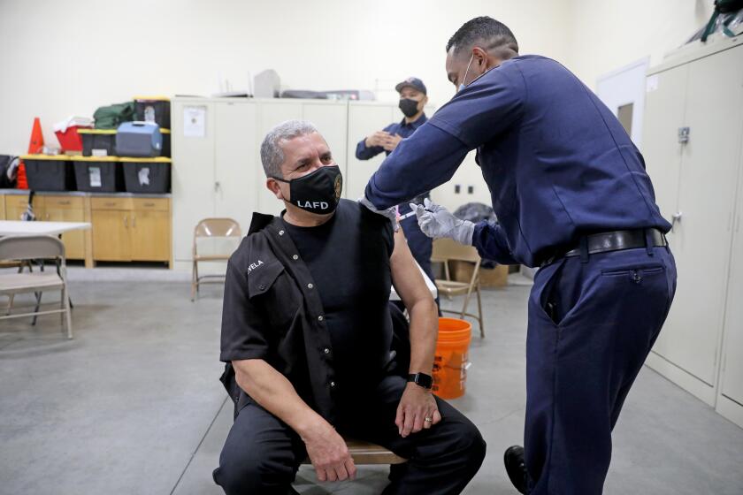 LOS ANGELES, CA - DECEMBER 28: John Novela, left, Los Angeles Fire Department (LAFD) fire inspector, receives a Moderna COVID-19 vaccination given by Mario Guillen, LAFD firefighter paramedic, at Station 4 on Monday, Dec. 28, 2020 in Los Angeles, CA. Mayor of Los Angeles Eric Garcetti and Ralph M. Terrazas, LAFD fire chief, were there to observe the rollout of the vaccination program. (Gary Coronado / Los Angeles Times)
