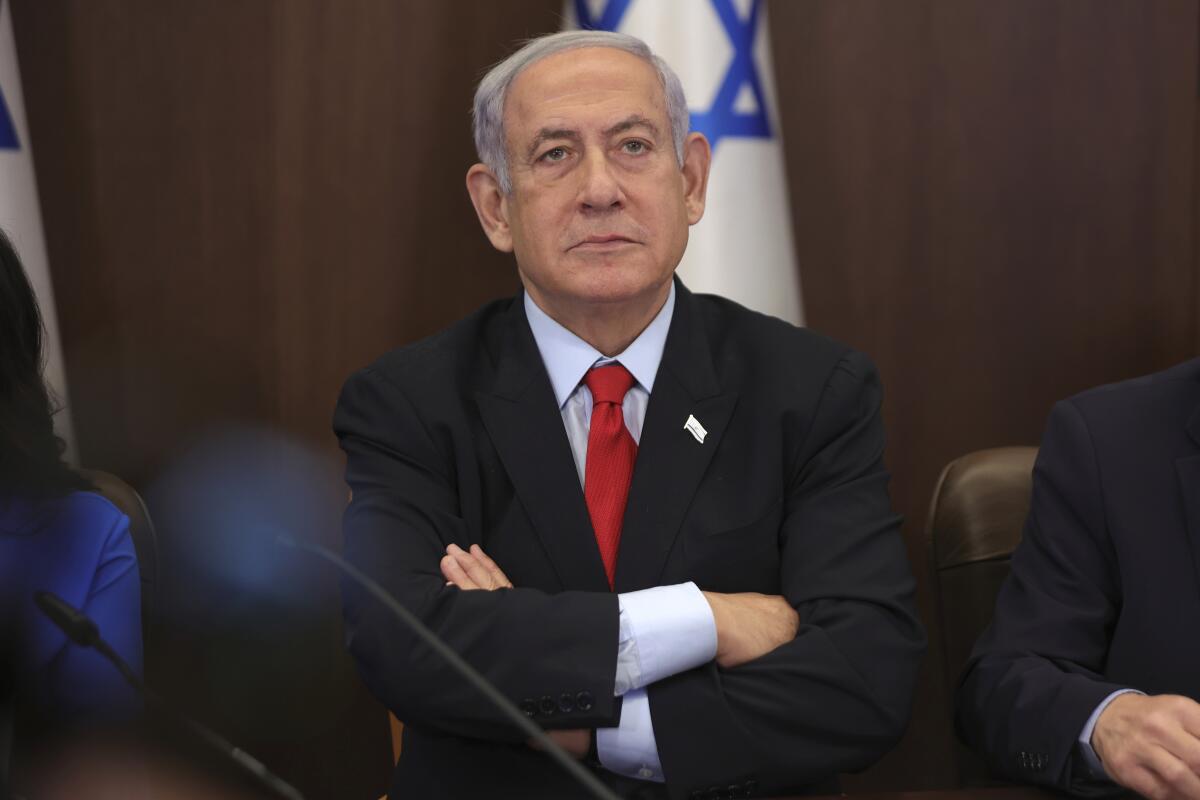 Israeli Prime Minister Benjamin Netanyahu sits in a suit with his arms crossed