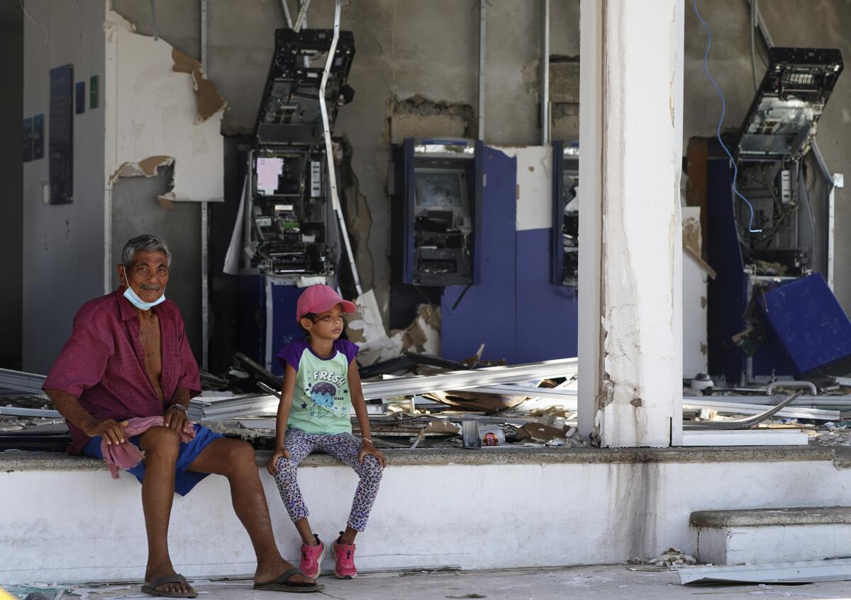 Residents sit at a bank lacking windows and with destroyed bank teller machines.