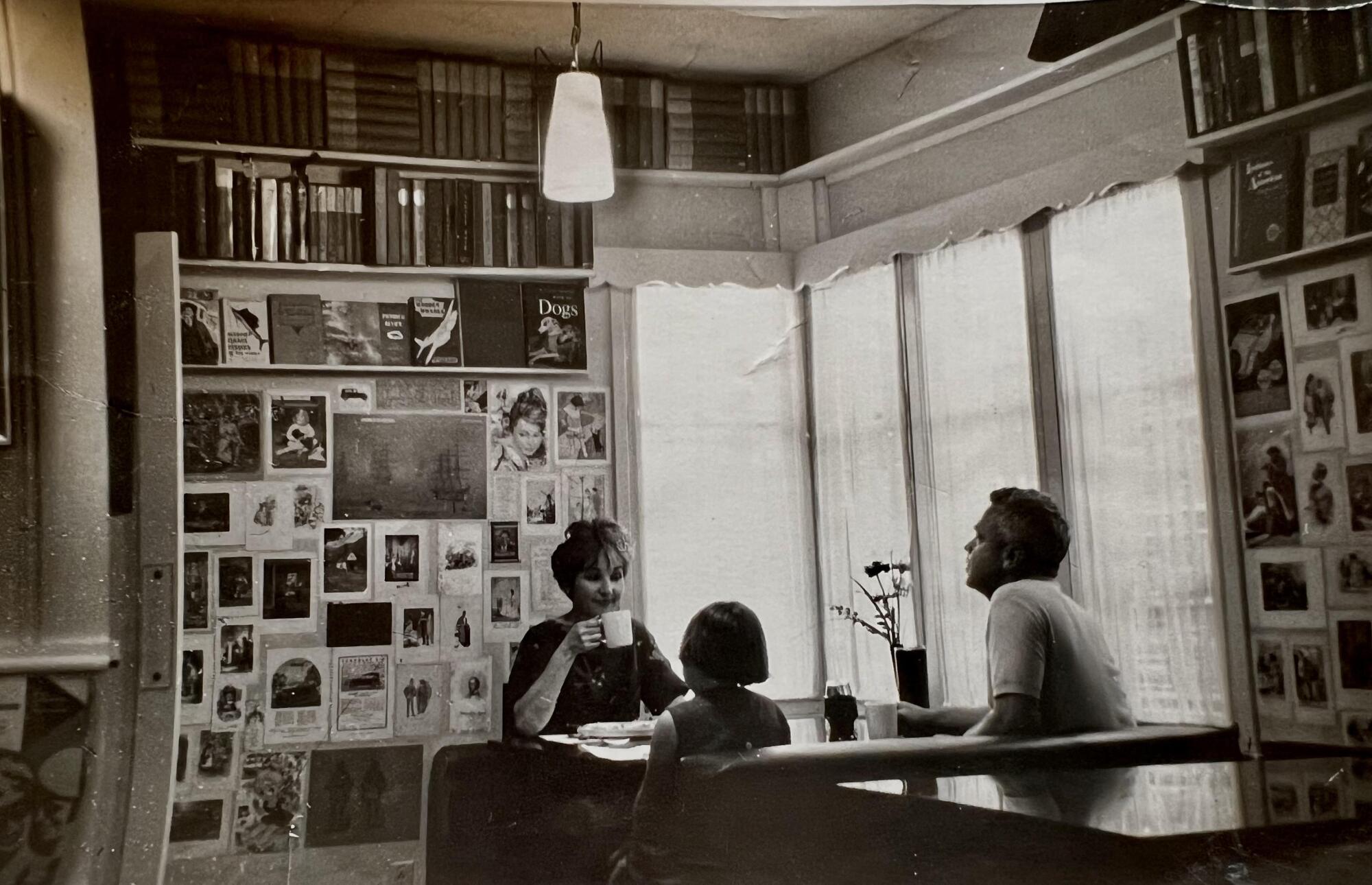 Three people sit at a table in a tearoom with postcards and books lining walls.