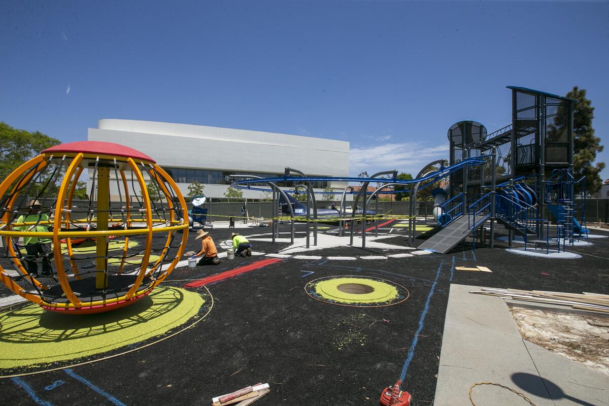 Contractors work on installing the rubber flooring for a new playground at Costa Mesa's Lions Park on Friday.