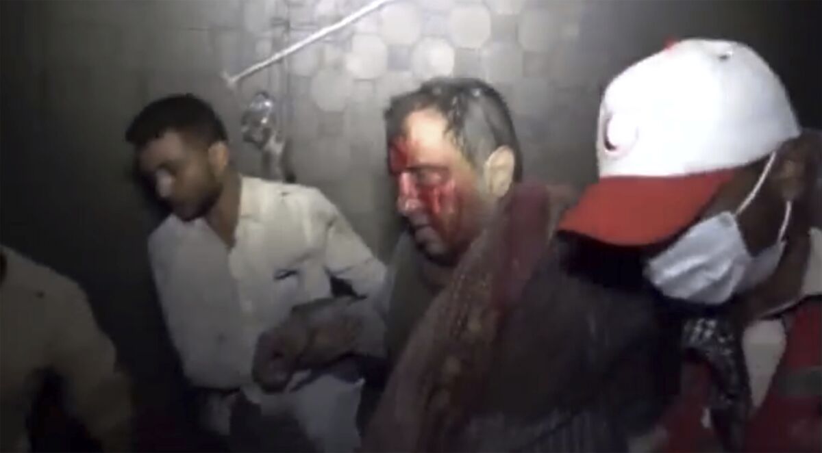 A man with blood on his face is rescued by two men. 
