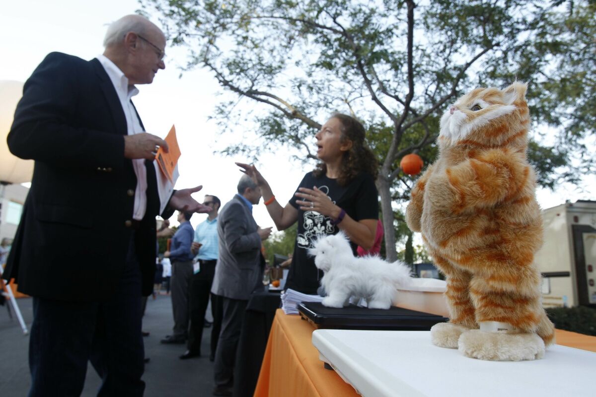 With a stuffed toy cat on the table, Sigalit Tsadok, center, of Tailio In-Home Cat Health Monitoring, talks to an attendee of Connect's New Office Grand Opening and 30th Anniversary Extravaganza.
