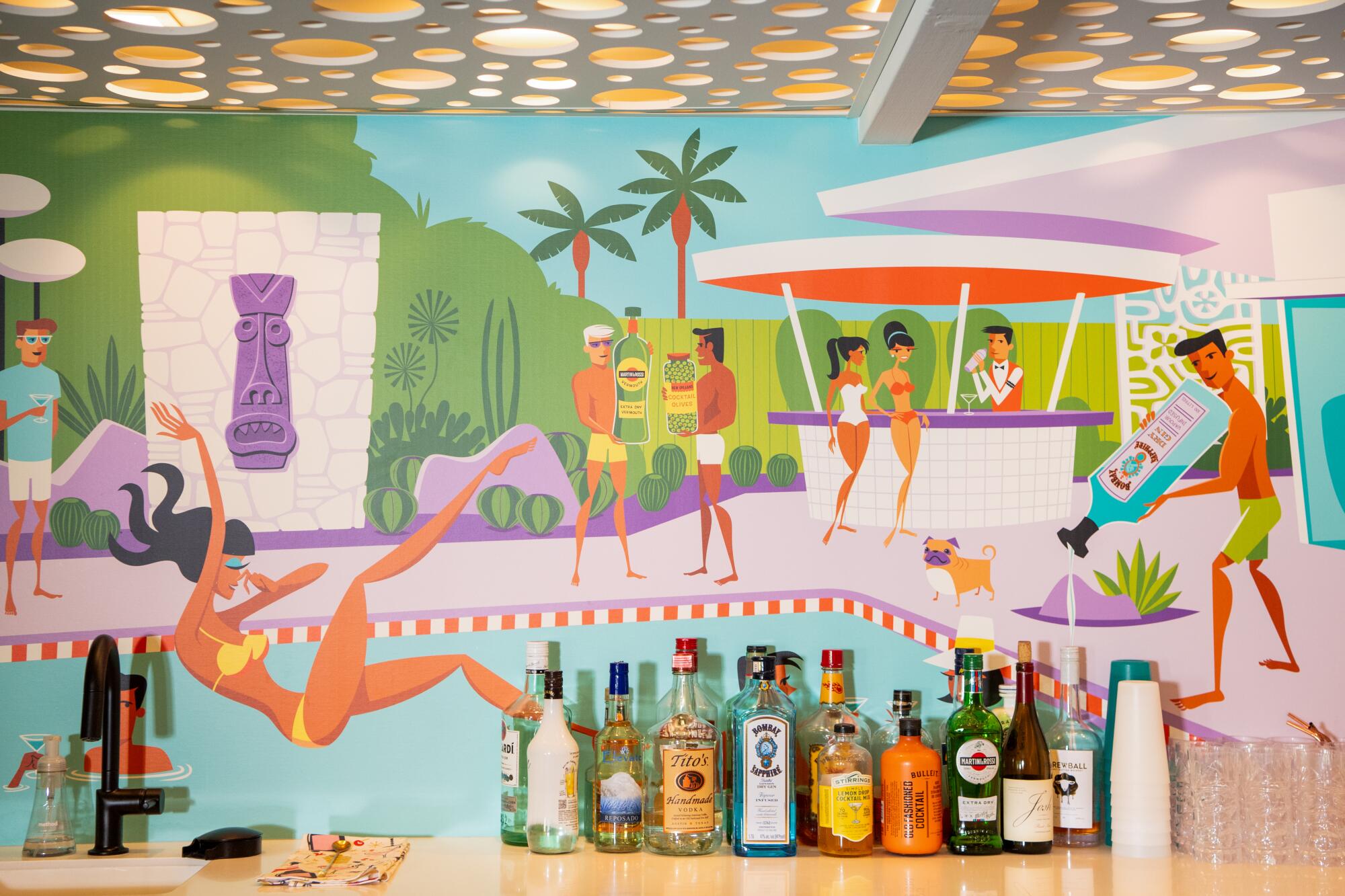 A mural behind a line of liquor bottles depicts a pool party with a woman falling into the water.