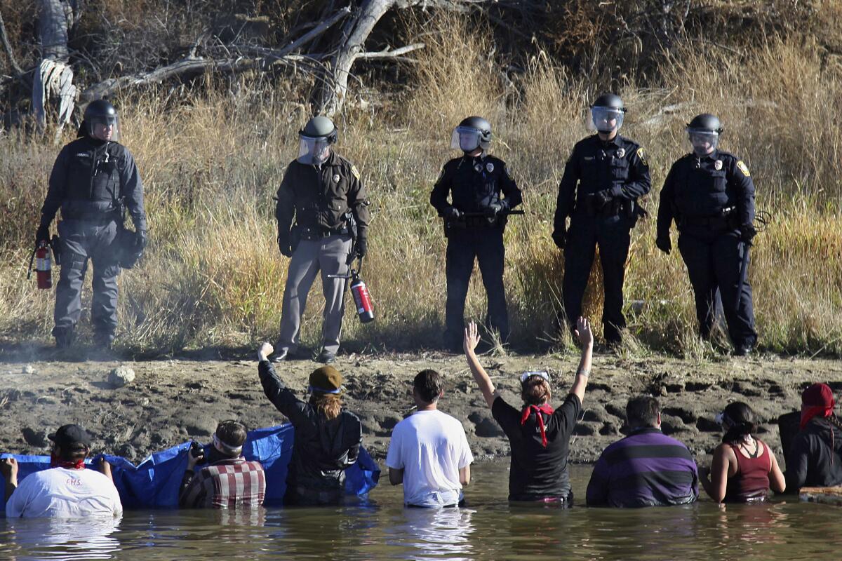 FILE - In this Nov. 2, 2016, file photo, dozens of protestors demonstrating against the expansion of the Dakota Access Pipeline wade in cold creek waters confronting local police, near Cannon Ball, N.D. Federal and state lawyers will meet in North Dakota next week to negotiate a settlement for money that the state claims it spent on policing protests against the Dakota Access oil pipeline. North Dakota filed a lawsuit against the U.S. Army Corps of Engineers in 2019, seeking to recover more than $38 million in damages from the monthslong pipeline protests almost five years ago. (AP Photo/John L. Mone, File)