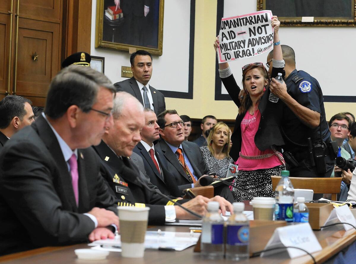 A demonstrator expresses her views as Defense Secretary Ashton Carter, left, and Martin Dempsey, chairman of the Joint Chiefs of Staff testify before the House Armed Services Committee on Capitol Hill.