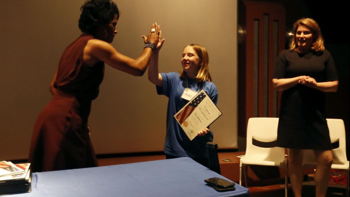 Annie Wilkinson, center, high-fives the FBI's Voviette Morgan, left, after accepting a certificate as Stephanie Christensen, right, of the U.S. attorney's office, looks on Friday at the Discovery Cube in Santa Ana.