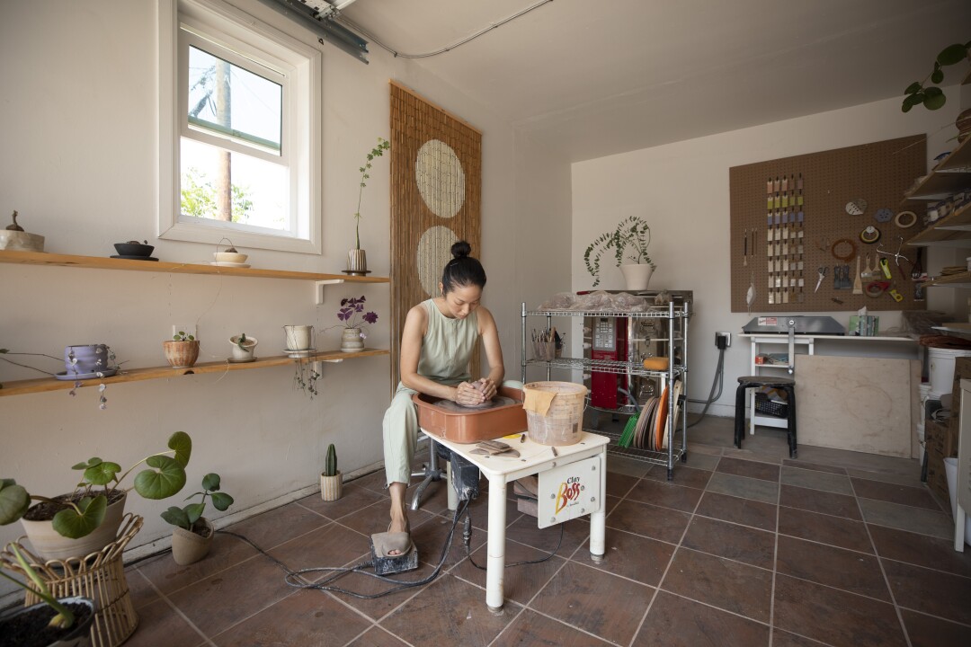 A woman in a studio shapes clay on her ceramics wheel