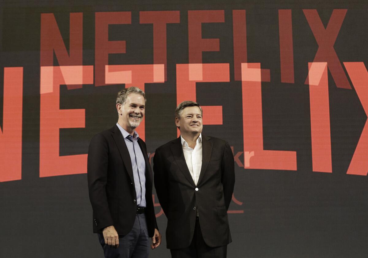 Reed Hastings and Ted Sarandos pose in front of the Netflix logo.