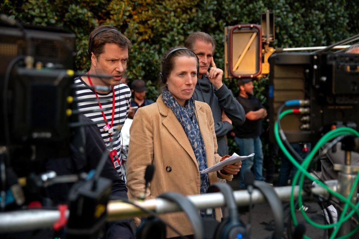 Both wearing headphones, a man and a woman watch a take on a movie set.
