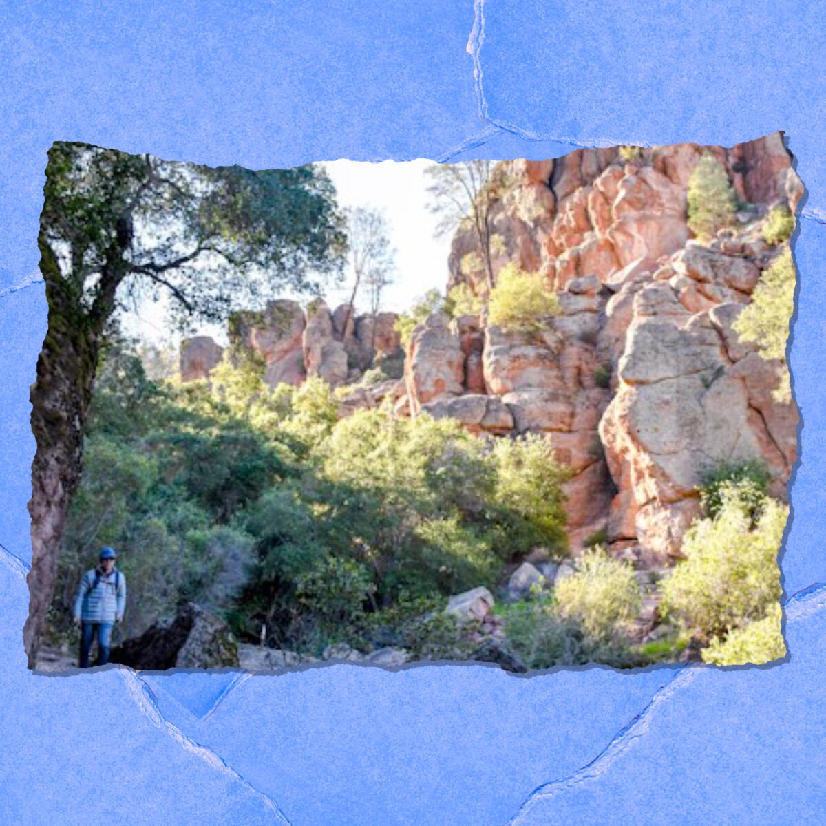 A person hikes next to large rock formations and greenery.