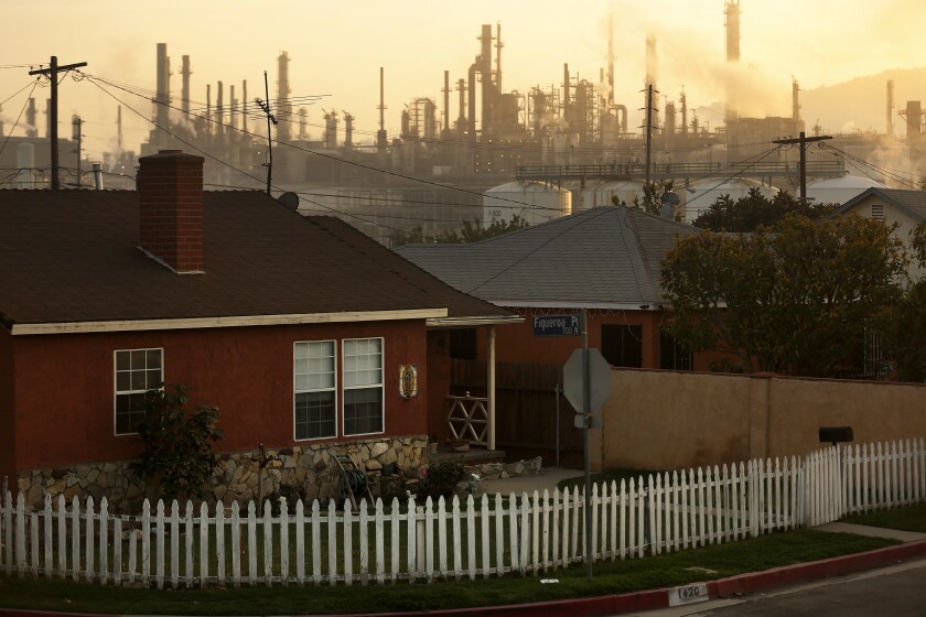 A refinery and smog loom behind houses in the Wilmington neighborhood of Los Angeles.