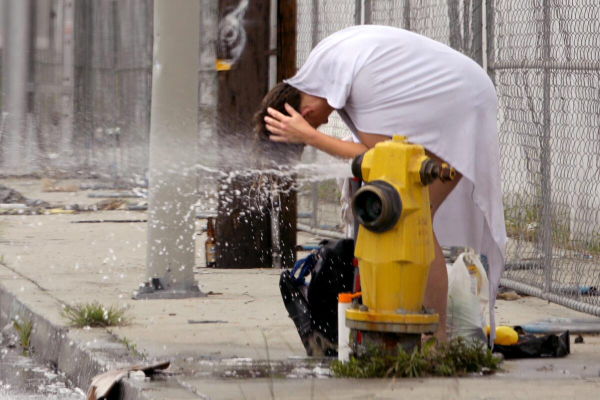 A woman bends over to rinse her hair in a jet of water from a hydrant.