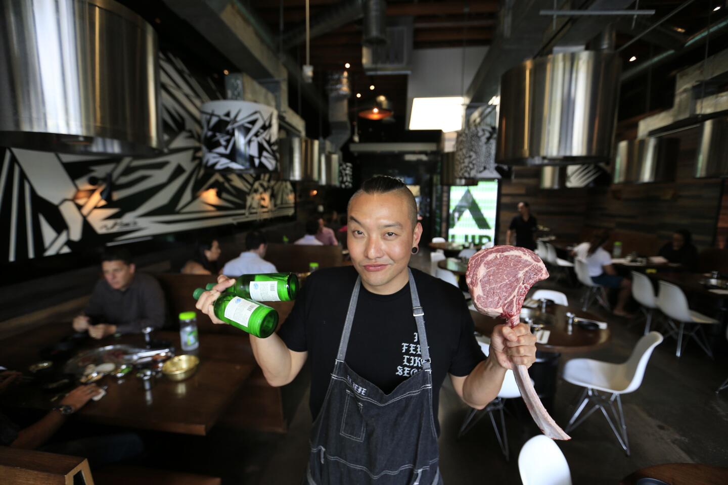 Chef Chris Oh holds beer and a 48-ounce tomahawk steak at Hanjip, a Korean barbecue restaurant.