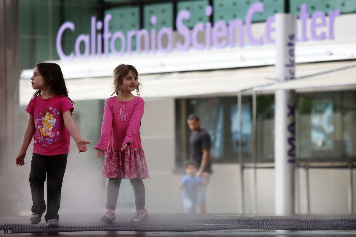 Two girls play in the mist from a fountain at the California Science Center.