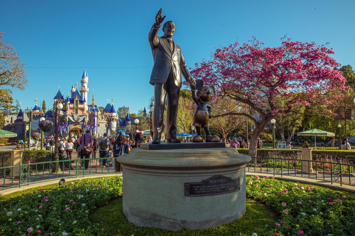 Statue of a waving man, holding the hand of Mickey Mouse, with Sleeping Beauty's Castle in the background 