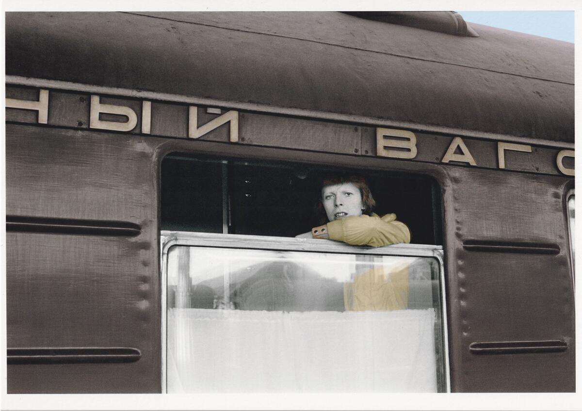 A man looks out the open window of a train, with Russian words in Cyrillic script above.